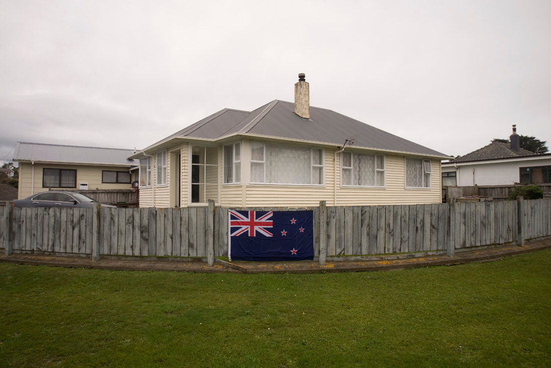 James Gilberd - Corner of Stephen St and Moorefield Rd, Johnsonville, May 2020, New Zealand under Covid-19 lockdown, urban landscape photography in New Zealand during Covid-19 Alert Level 2, New Zealand flag on fence in Johnsonville Wellington, photograph by James Gilberd for online photography exhibition A Month of Sundays - Responses to the Covid-19 lockdown in New Zealand, Photospace Gallery contemporary New Zealand photography