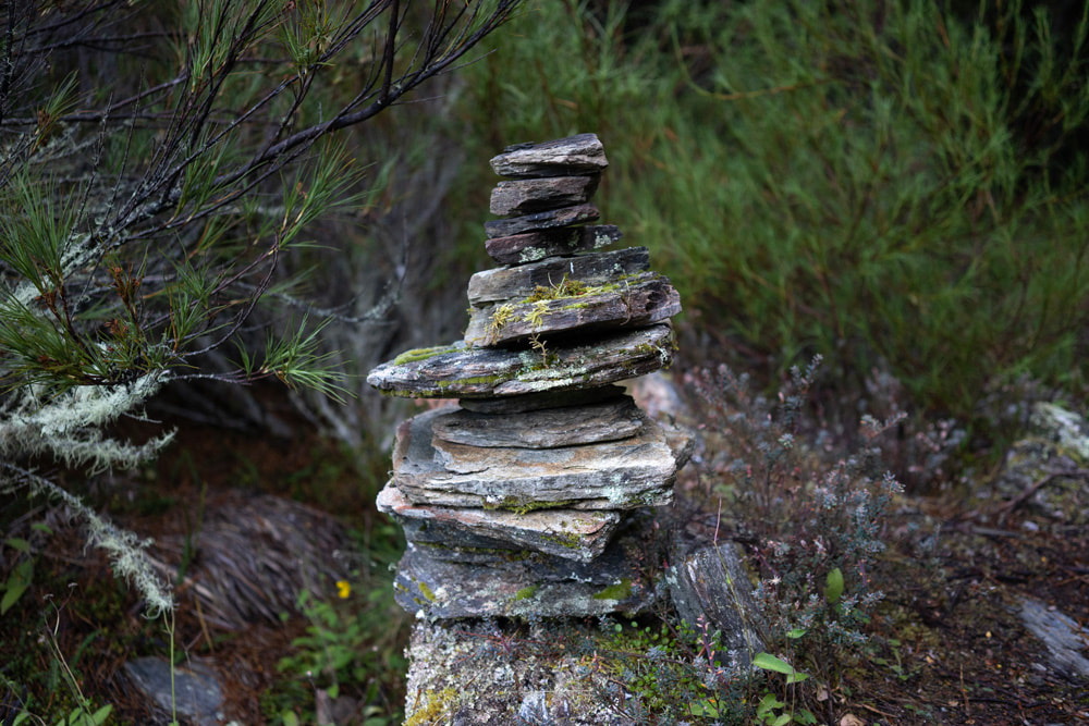 Jake Giles 'Pilgrimage' exhibition poster, Photospace Gallery 12 May-3 June 2023, Wellington NZ , photo of trail marker of stacked stones, tramping the South Island Aotearoa New Zealand, walking and cycling journey around Aotearoa New Zealand, New Zealand South Island photographs during while walking and cyling, New Zealand contemporary fine art photography